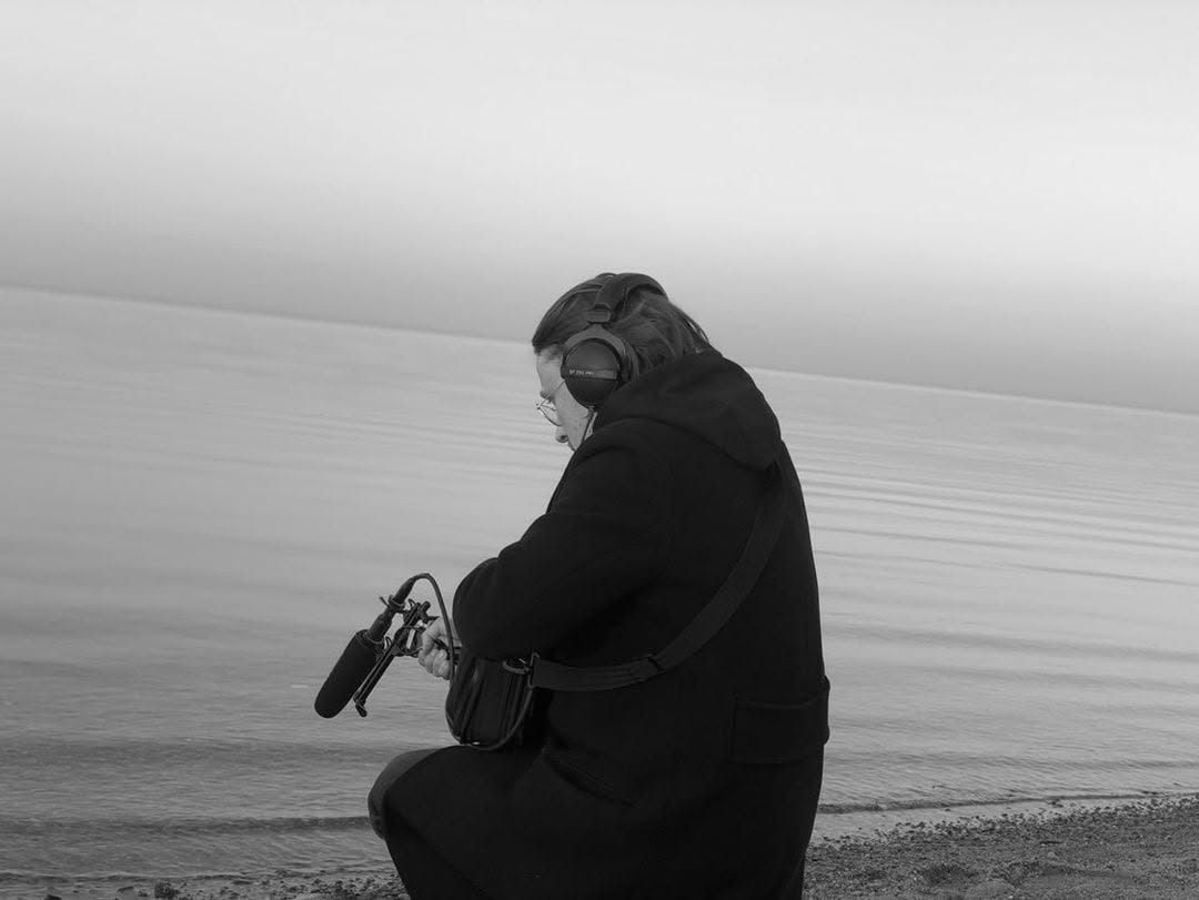 Cezary Cybulski recording on location at the shore, with a field recorder and headphones.